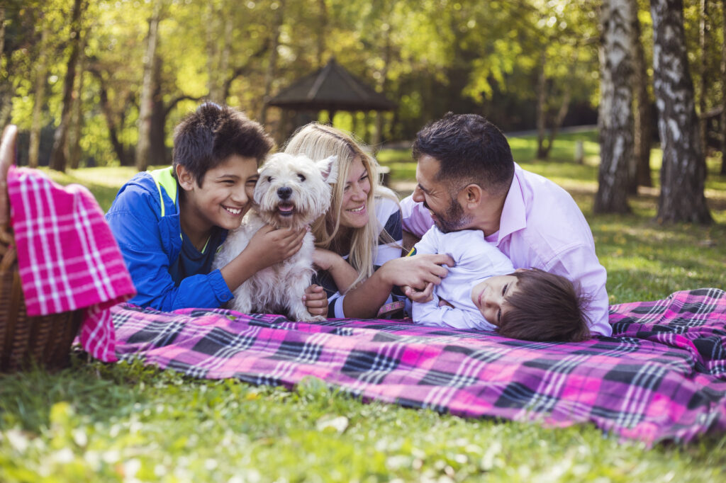 Mixed-race family enjoying in public park with cute white dog